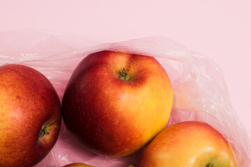 Red apples in a transparent plastic bag on a pink paper background. Concept of earth day, zero waste and recycling