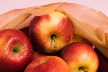 Red apples in a reusable fruit and vegetable bag on a pink paper background. Concept of earth day, zero waste and recycling