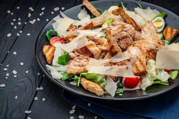 Fresh caesar salad in white plate on dark wooden table. Top view.