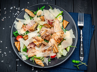 Fresh caesar salad in white plate on dark wooden table. Top view.