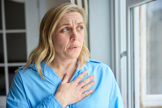 Menopausal Mature Woman At Home Standing By Window Suffering With Heart Palpitations