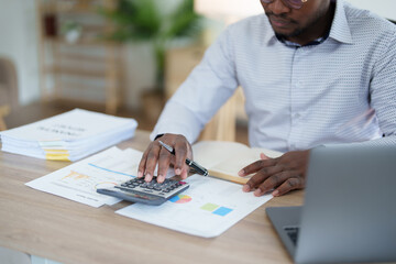 middle age man American African using calculator for calculating and laptop computer with planning working on financial document, tax, exchange, accounting and Financial advisor