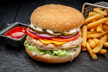 Burger with chicken cutlet and french fries on a dark background