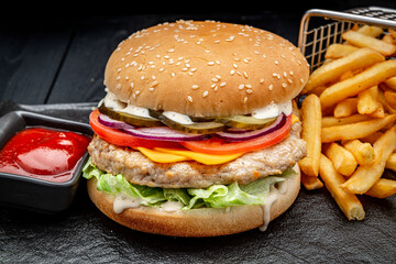 Burger with chicken cutlet and french fries on a dark background