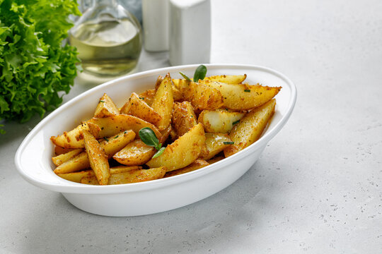 Baked potato wedges in white baking dish. Roasted potatoes with herbs and spices. Dinner idea. Copy space for text.