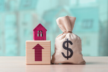 Money bag with dollar symbol and house model on wooden cube with arrow up. Concept of real estate and rent cost increase