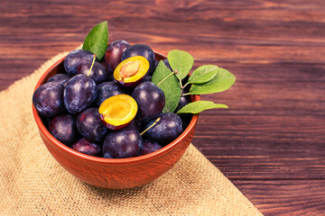 Fresh blue plums in a bowl on a wooden background. Copyspace.