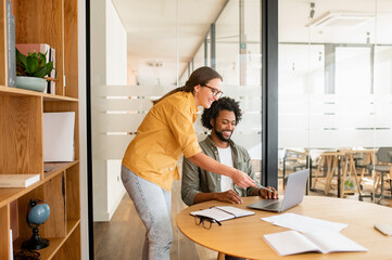 Pair of friendly colleagues work in office. Young guy and girl in glasses are working with a laptop...