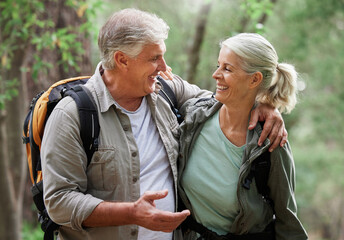Talking, hiking and happy senior couple on nature adventure in forest, woods and mountain for exercise. Fitness, retirement and elderly man and woman smile, in conversation and trekking for wellness