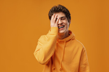 Young man wearing casual yellow hoody puts hand on face facepalm mistaken on yellow background