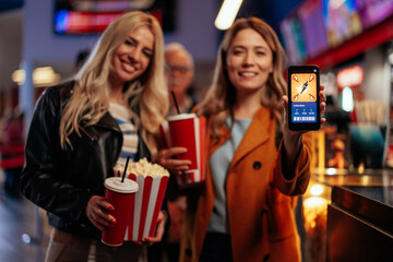 Joyful friends with mobile app in cinema.