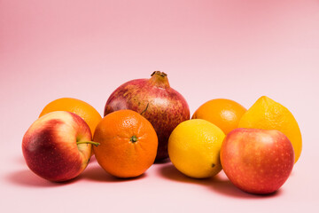 Fruits of pomegranate, lemon, apple, oranges and tangerine on a pink background. Delicious fruits on a bright background.