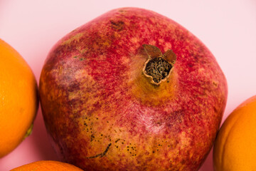 Juicy pomegranate and oranges on a pink background close-up. Delicious fruits on a bright background.