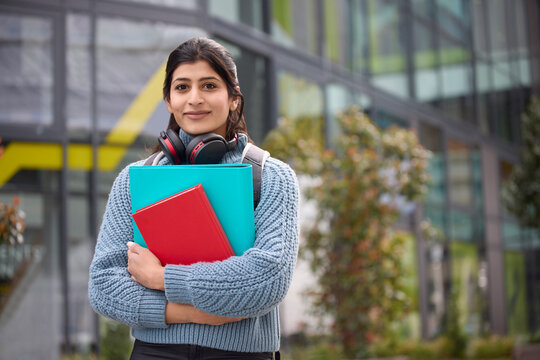 Female College Or University Student Outside Campus Building Wearing Wireless Headphones