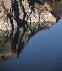 Rocky shore on the lake and reflection in the water in autumn at dawn, cliff break above the water