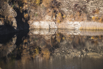 Rocky shore on the lake and reflection in the water in autumn at dawn, cliff break above the water