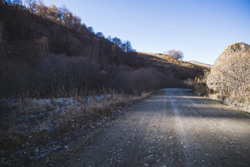 A dusty road in the autumn mountains on a sunny November morning goes into the distance