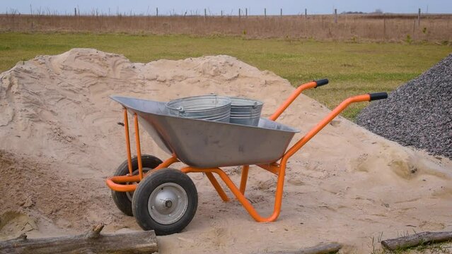 Putting sand with a shovel or spade outdoors into metallic buckets standing on a hand cart