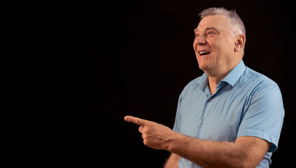 Handsome elderly man with gray hair poses against a black background with copy space and smiles cheerfully.