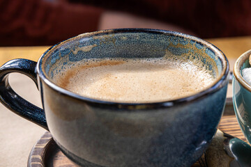 Blue Ceramic Cup of Hot Cappuccino with Foam on Wooden Cafe Table. Beautiful Latte with bubble Froth. Trendy Authentic Modern Porcelain Set. Pottery Handmade Coffee Mug Served with a Sugar Bowl
