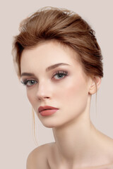 Obraz premium Close-up shot of a young European woman with makeup and bouffant hairstyle. Beautiful girl with her hair pulled back is isolated on a beige background. Modern hairstyle on woman. Front view.