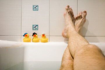 Legs of man relaxing in the bath and yellow ducks