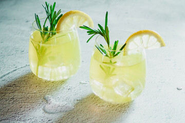 Cold cocktail, lemonade with lemon sliced, rosemary plant on white concrete background. Drink photo