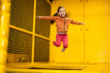 Little girl kid jumping on trampoline at yellow playground park. Child in motion during active...