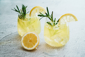 Cold cocktail, lemonade with lemon sliced, rosemary plant on white concrete background. Drink photo - obrazy, fototapety, plakaty