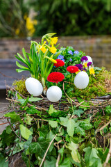 Beautiful Easter decoration in a wicker basket with white Easter eggs and colorful spring flowers