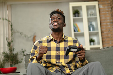 Young happy African guy playing video game at home. Man holding joystick and playing video games.