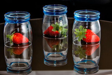 three strawberries covered by glass basins reflecting in the background