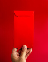 A red envelope holding by hand isolated on red background, vertical style. Hongbao packet for lucky money gift in Chinese lunar, new year on January month, wedding red packet.