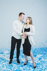 Young happy married couple hugging in blue confetti. A couple in love rejoices and has fun. Gender photo session