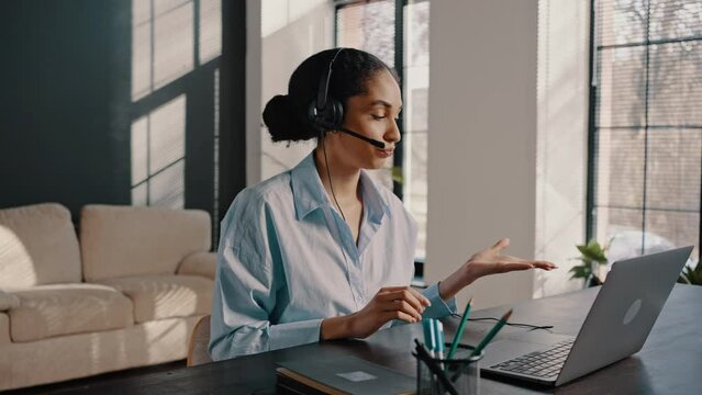 Confident African American woman wearing audio headset, sitting at laptop at online business meeting