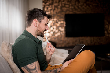 Fototapeta na wymiar Handsome young man with a sleeve tattoo using digital tablet at home.