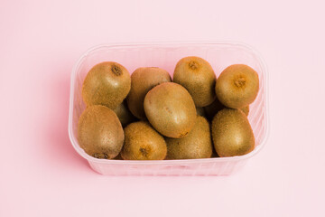 Kiwi in plastic packaging on a pink background. Concept of earth day, zero waste and recycling.