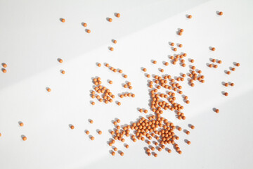 Many little orange balls scattered on a white background in the bright light, dropping shadows. Geometrical abstract futuristic wallpaper with lots of small round particles