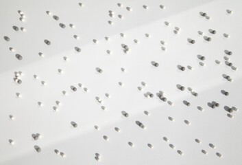Many little white and gray balls scattered on a white background in the bright light, dropping shadows. Geometrical abstract futuristic wallpaper with lots of small round particles