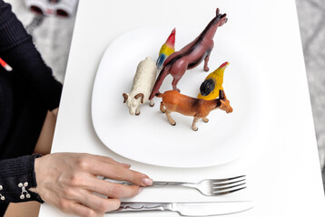 farm animals plastic toys in white plate and woman female hands holding knife and fork pretending to eat.eat meat concept domestic animals.being vegetarian vegan be like.food nutrition