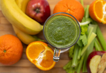 healthy smoothie in glass and fruits all around on wooden board kitchen table and background.slim fit weight loss take natural vitamins.bio tangerine celery spinach kiwi and apple.mashed fruits 