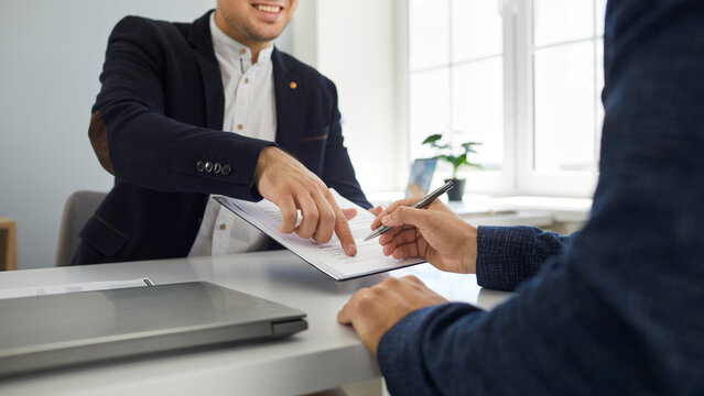 Two happy young people make a business deal and sign a contract agreement in the office. Friendly, smiling agent shows his client where to put a signature. Cropped shot. Banner background