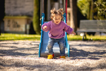 Sweet caucasian little toddler girl with two tails having fun smiling widely sliding down the...