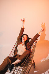 Beautiful elegant young woman model in nice stylish brown suit posing in shopping cart on gray background. Young elegant woman in a suit