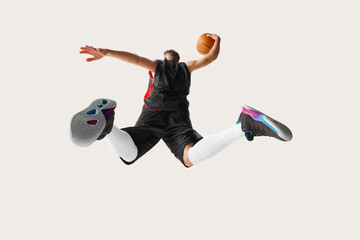 Portrait of male professional basketball player jumping and throwing ball into the basket over white background