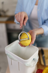 Female hands peeling off potato and throwing peels in a compost bin for decomposition. Woman...