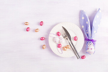 Easter table setting. White plate with a napkin folded in the shape of a rabbit, Easter and chocolate eggs on a pink background. Happy Easter holiday concept. Top view, flat lay