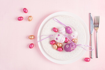 Happy Easter. Table setting for Easter holiday. Easter eggs, flower and cutlery on pink background. Top view, flat lay