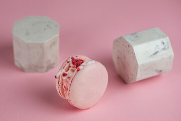 Pink French macarons with cream and freeze-dried raspberries on a pink background on marble stands. A stylish concept for coffee shops, confectioners, bakeries.