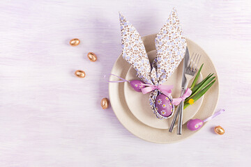 Easter table setting. White plate with a napkin folded in the shape of a rabbit, Easter and chocolate eggs on a pink background. Happy Easter holiday concept. Top view, flat lay